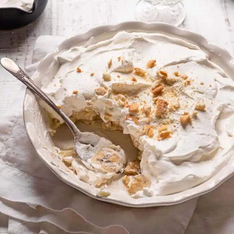 Banana pudding in a pie dish topped with vanilla wafers with a spoon in the front.