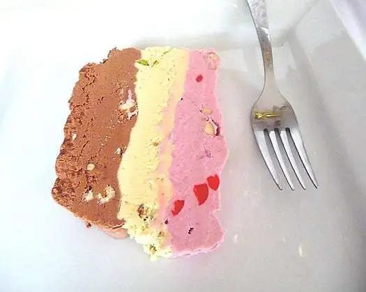 Slice of spumoni ice cream terrine on a white plate with a fork.