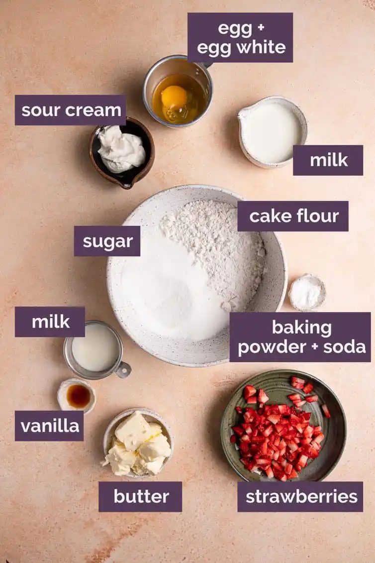Ingredients for strawberry cupcakes on a pink counter with purple labels.