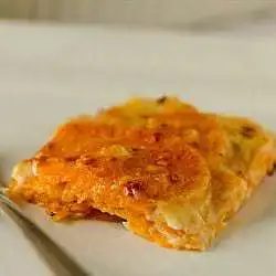 Serving of sweet potato gratin on a white plate with a fork.