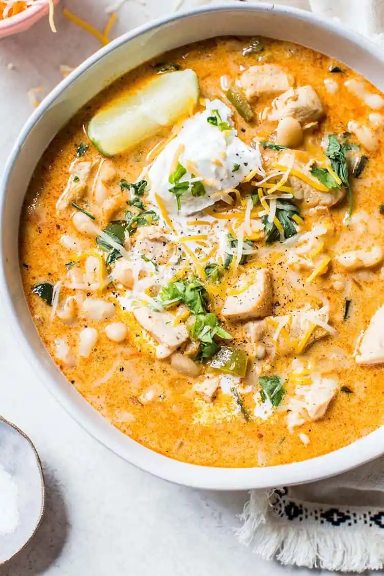 A close up shot of a bowl of white chicken chili topped with sour cream, cilantro and a lime wedge.