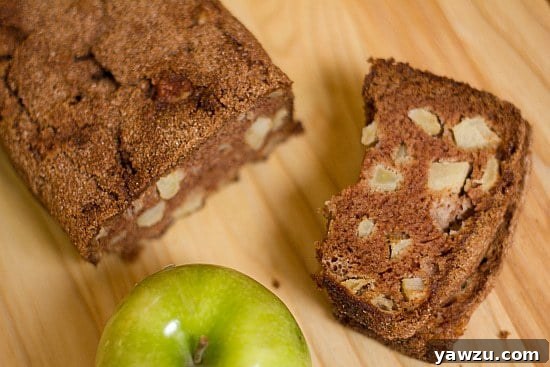 Overhead image of a loaf of apple cinnamon bread and one slice of it on a wood surface, highlighting its golden crust and soft interior.