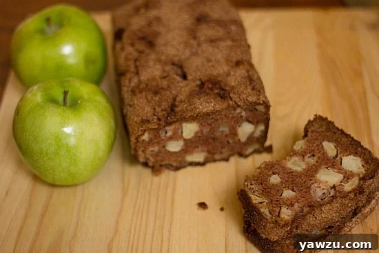 A perfectly baked loaf of apple cinnamon bread with a golden-brown crust, accompanied by a single slice on a rustic wood surface, inviting you to taste.