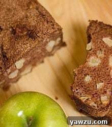 Overhead image of a loaf of apple cinnamon bread and one slice of it on a wood surface.