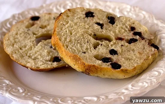 A vibrant blueberry bagel, freshly baked and cut in half, showcasing its dense, chewy crumb flecked with sweet blueberries, presented on a white plate.