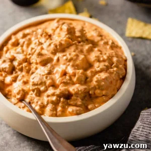A top down photo of a white bowl with creamy sausage dip with a silver spoon on the left side on the bowl.