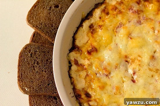 Overhead image of a baked hot reuben dip in a white baking dish, surrounded by various crackers and rye bread for serving.