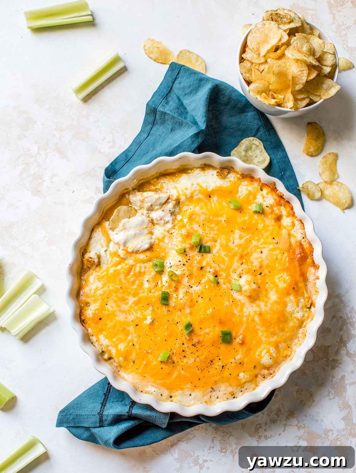 Buffalo chicken dip in a round white baking dish with potato chips and celery nearby.