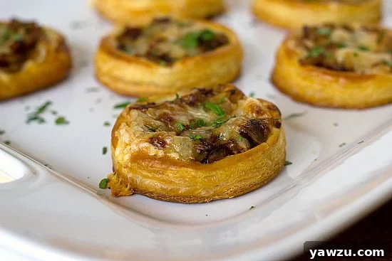 Close-up side view of baked caramelized onion, mushroom, and gruyere tartlets, showing flaky pastry and melted cheese.