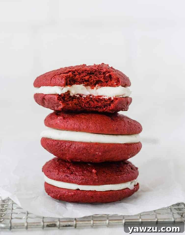 A stack of three perfectly baked red velvet whoopie pies, showcasing their vibrant red color and creamy white filling.