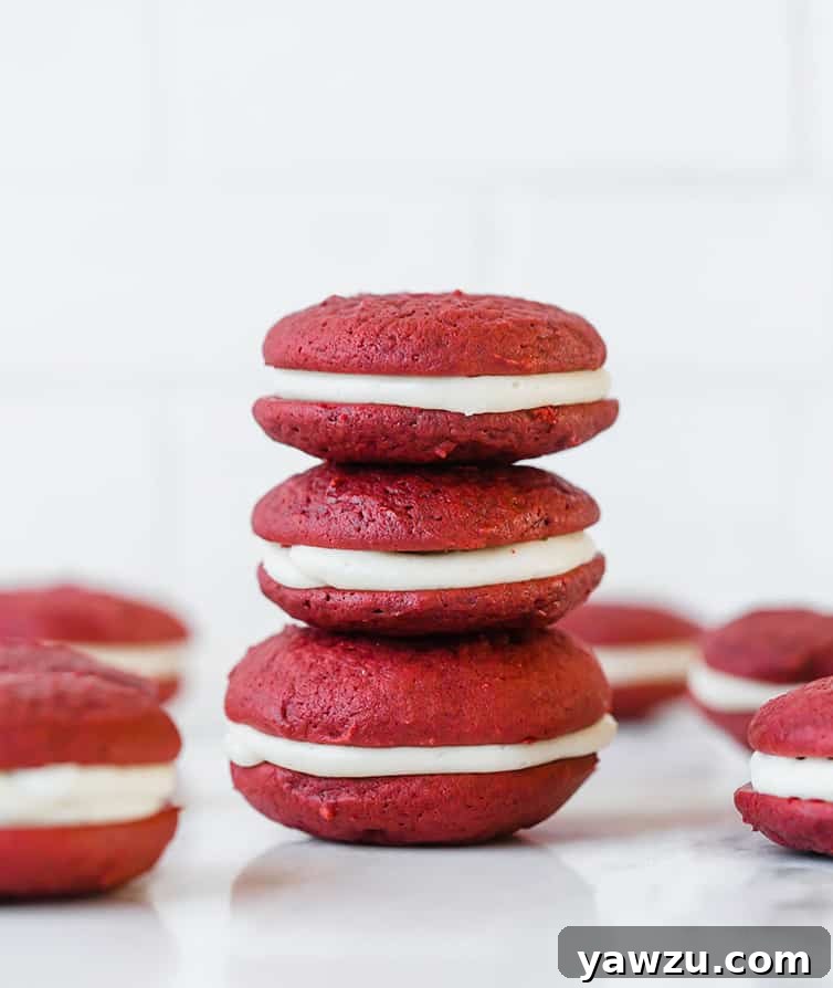 A beautifully arranged stack of three red velvet whoopie pies, perfectly showcasing the light, fluffy texture of the cakes and the generous cream cheese filling.