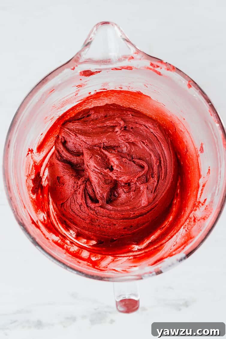 A glass mixing bowl filled with vibrant red velvet cookie batter, ready for baking.