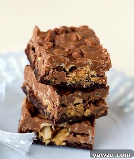 Stack of 3 decadent Peanut Butter Cup Crunch Brownie Bars on a pristine white plate, showcasing their rich layers of chocolate, peanut butter, and crunchy topping.