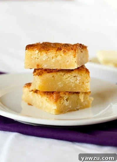 Stack of 3 white chocolate coconut brownies on a white plate, invitingly arranged.