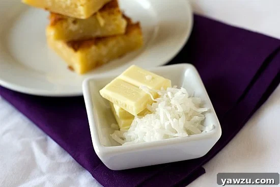 White chocolate squares and shredded coconut in a square white bowl, ingredients for baking.