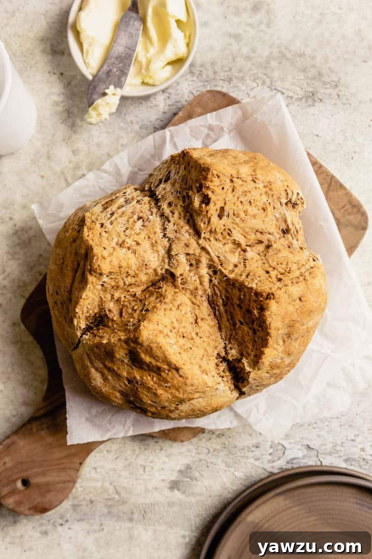 A wooden cutting board topped with parchment paper and a loaf of Irish brown bread with a bowl of butter and a butter knife at the top.