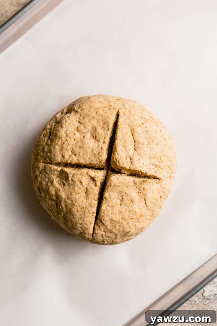 Irish brown bread dough on a parchment paper lined baking sheet with a cross cut in the top of the loaf.