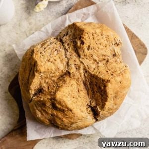 A loaf of Irish Brown Bread on a piece of parchment paper on a wooden cutting board.