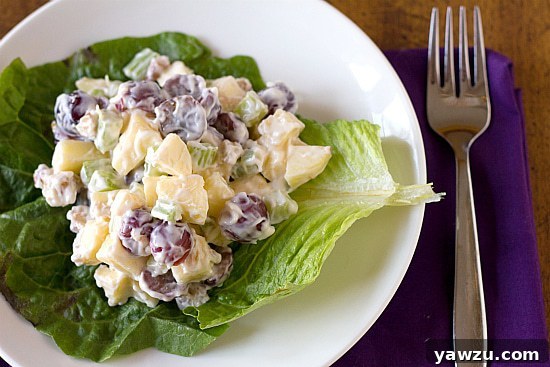 A vibrant serving of classic Waldorf salad on a bed of fresh lettuce, elegantly presented on a white plate. This refreshing dish features crisp apples, sweet grapes, crunchy celery, and toasted walnuts, all tossed in a creamy, tangy dressing.
