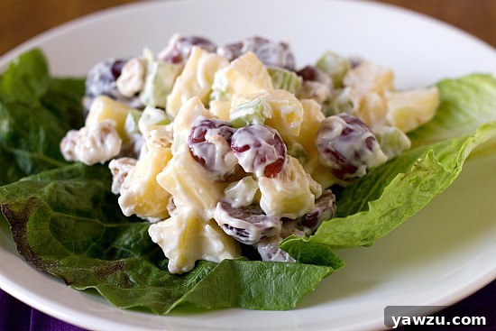 Close-up shot of a single serving of Waldorf salad, generously portioned on a crisp lettuce leaf and placed on a pristine white plate, highlighting the vibrant colors and appealing textures of the fruit and nut medley.