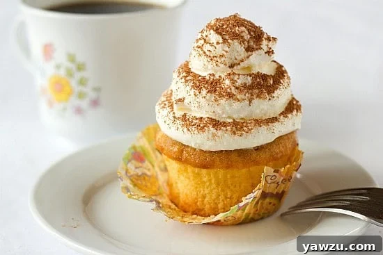 A single tiramisu cupcake elegantly presented on a white plate with a fork nearby.