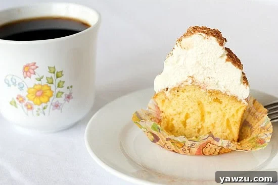 A tiramisu cupcake cut in half on a white plate, revealing its moist interior and distinct layers.