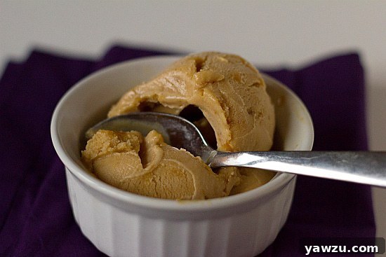 A spoonful of salted caramel ice cream showing bits of praline, in a white bowl.