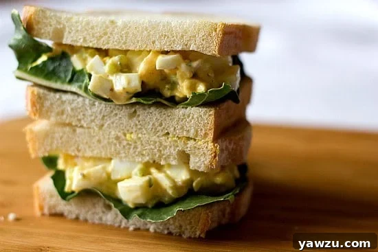 Stack of 2 egg salad sandwiches on a wood board.