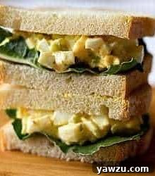 Stack of 2 egg salad sandwiches on a wood board.