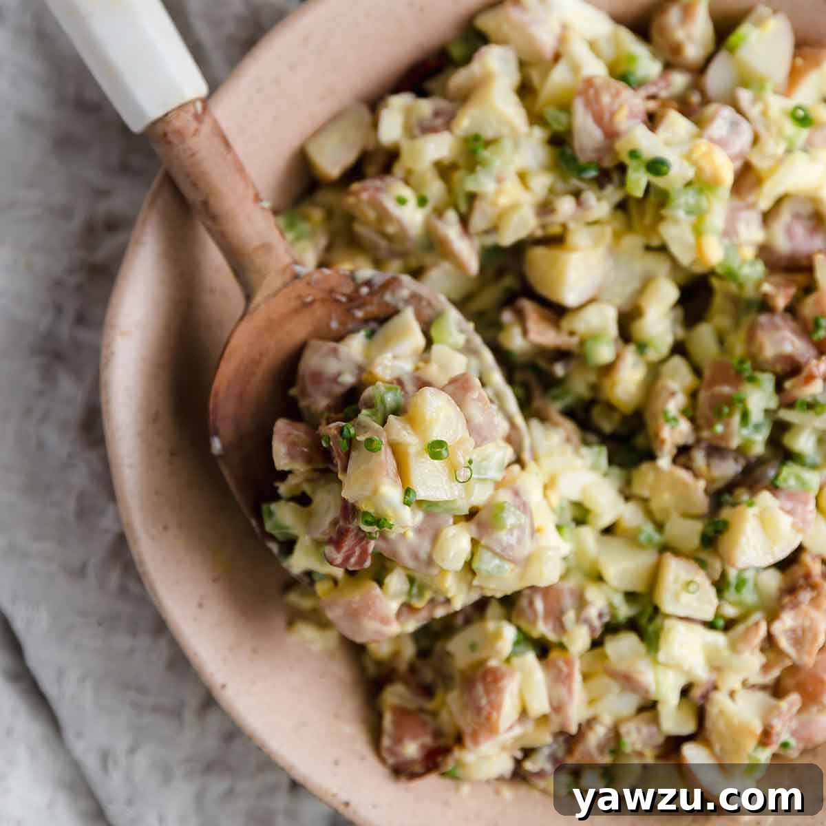 Close up photo of a scoop of potato salad on a wooden serving spoon.