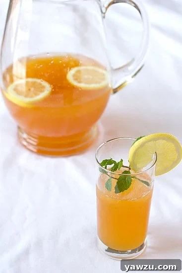 Ginger tea lemonade in a glass garnished with a lemon round and a glass pitcher of ginger tea lemonade.