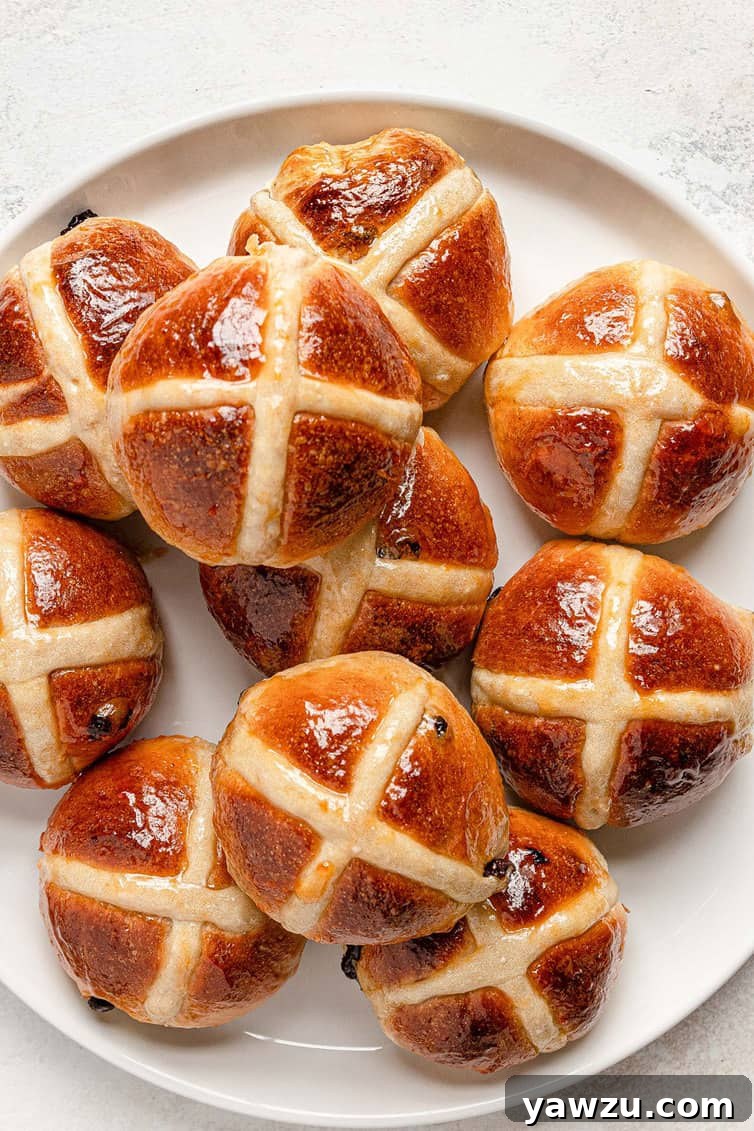 A white plate piled high with golden-brown hot cross buns, ready to be served.