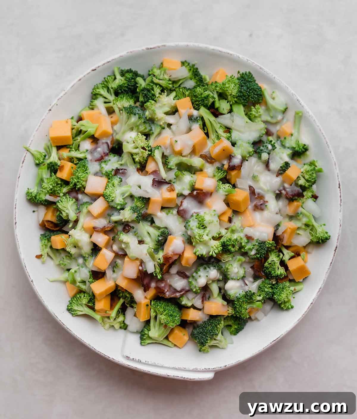 Overhead photo of broccoli salad in a rustic white bowl, garnished with a sprig of fresh parsley.