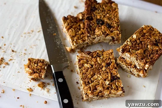 Freshly baked homemade granola bars, cut into neat squares, arranged on a piece of parchment paper on a wooden cutting board, with a knife resting nearby.