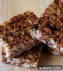 Three golden-brown crunchy granola bars artfully arranged on a light wooden surface, highlighting their inviting texture and readiness to be enjoyed as a perfect snack.