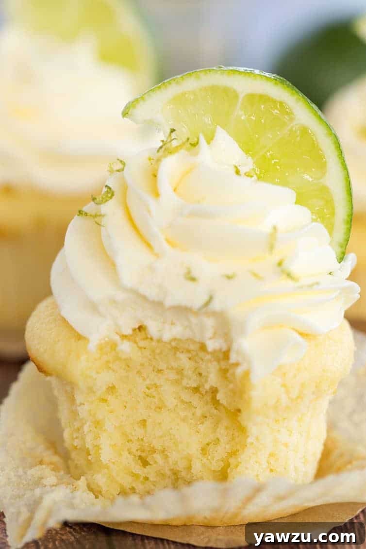 Margarita Cupcakes - A vanilla cupcake with vanilla frosting, lime zest and a lime wedge has a bite taken out of it.