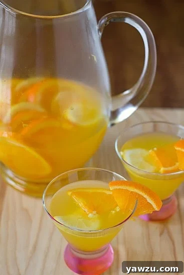 A pitcher of white sangria with citrus slices, accompanied by two glasses of sangria, against a bright, inviting background.