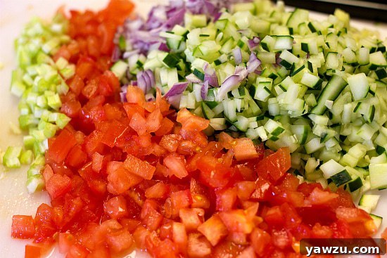 A colorful array of freshly chopped vegetables, including red onion, cucumber, Roma tomatoes, and zucchini, ready for gazpacho preparation.