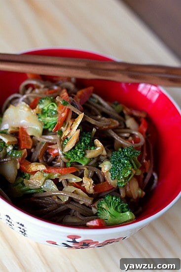 A serving of soba noodle stir fry with chopsticks in a red bowl.
