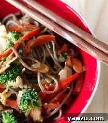 Soba noodle stir fry in a red bowl with chopsticks.