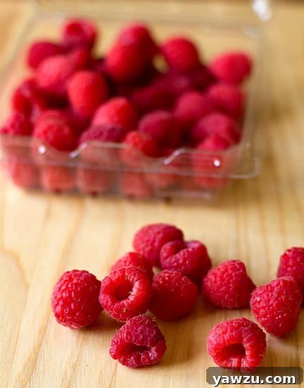 A close-up shot of fresh, plump raspberries scattered on a rustic wooden surface, highlighting their natural beauty.