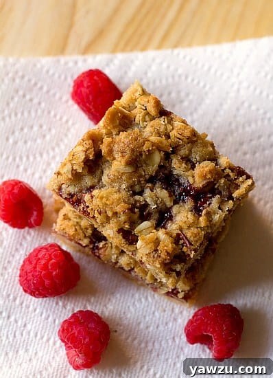 An inviting overhead view of a stack of golden-brown raspberry streusel bars, showcasing their crumbly topping and fruity filling, presented on a paper towel.