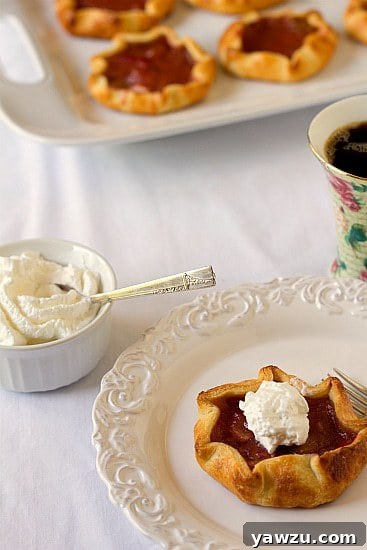 Delicious rhubarb pie tartlet, golden brown crust with a bubbly pink rhubarb filling, served on a white plate with a fork and a side of creamy whipped cream.