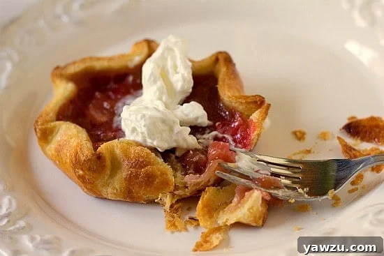Close-up of a single rhubarb pie tartlet on a white plate, showcasing the beautifully crimped cornmeal crust and the inviting pink filling, ready to be enjoyed.