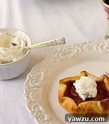 Rhubarb pie tartlet on a white plate with a fork and whipped cream in a white bowl with a spoon.