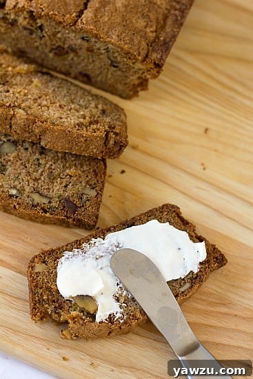 Overhead image of slices of zucchini pineapple bread on a wood cutting board with butter spread on a slice with a knife.
