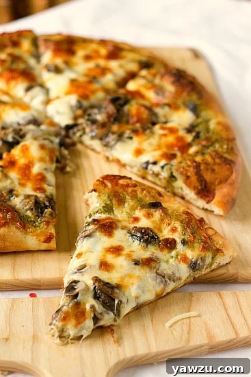 Close-up of freshly baked portobello pesto pizza slices on a wooden board, showcasing the melted cheese and vibrant toppings.