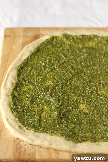 Pizza dough on a wooden board, now evenly spread with aromatic green pesto, creating a flavorful base.