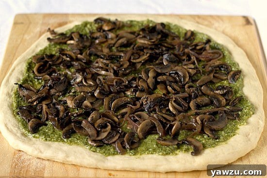 Pizza dough topped with vibrant pesto and a generous layer of sautéed portobello mushrooms and red onions.