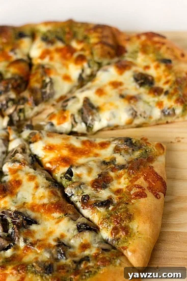 Perfectly baked slices of portobello pesto pizza, glistening with melted cheese and fresh pesto, arranged on a wood cutting board.